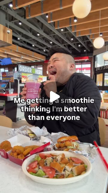 I laugh while holding a purple smoothie behind a table filled with Sheetz sandwiches, sides, and a salad.