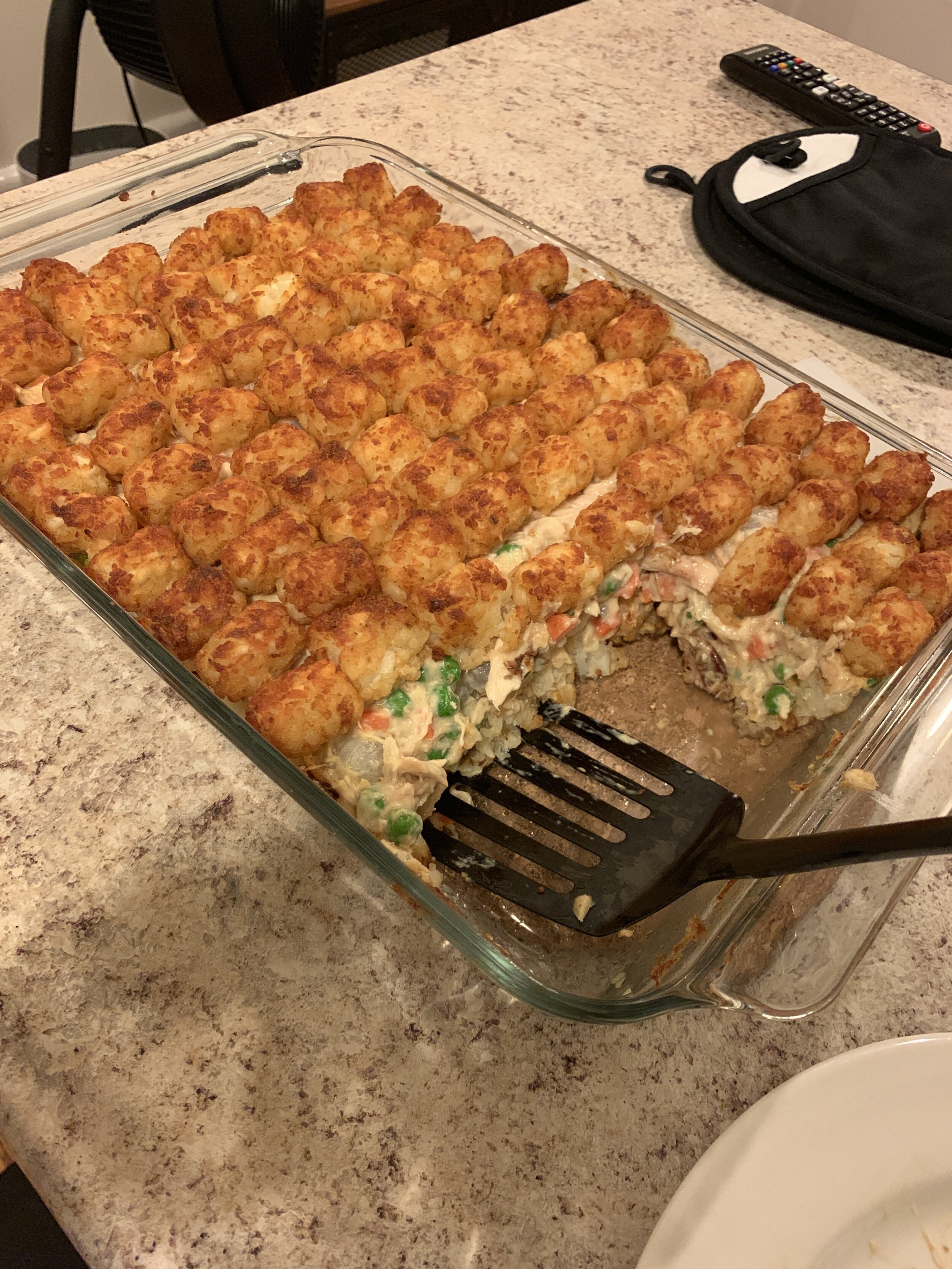 A glass baking dish of chicken pot pie covered with browned tater tots, with one serving removed.