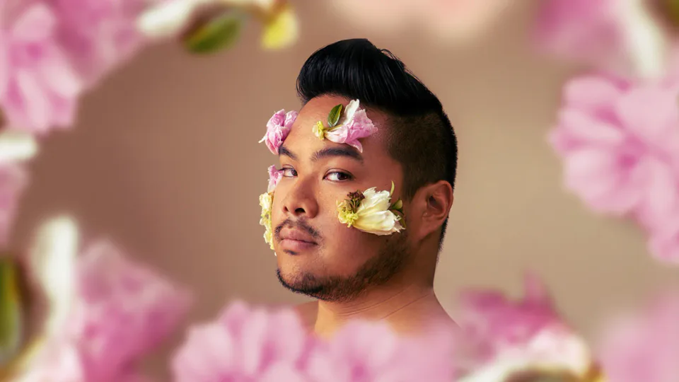 RV Mendoza framed by pink and white flowers, with small blossoms arranged across his face.