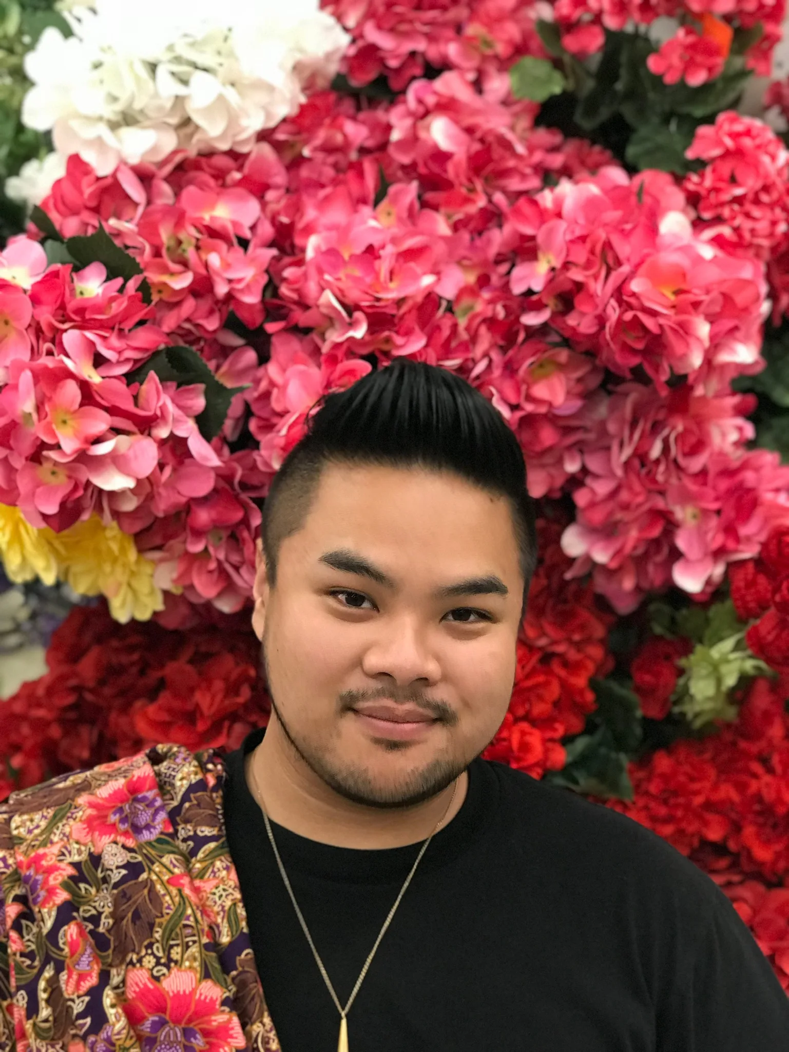 RV Mendoza smiling in front of a wall covered with bright pink, red, and white flowers.
